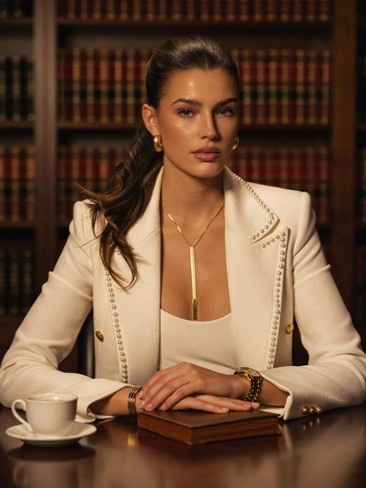 Advogada de blazer claro à mesa, com biblioteca ao fundo